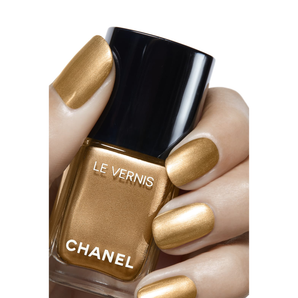 Chanel nail polish bottle with gold nail polish on a white background