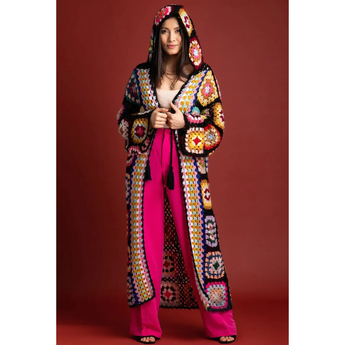Woman wearing a colorful, patterned coat and pink pants on a red background