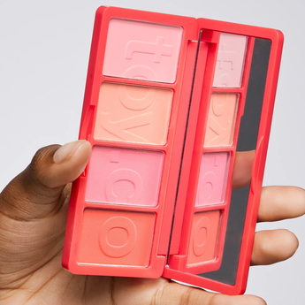 Makeup palette with blush shades held by a hand against a gray background